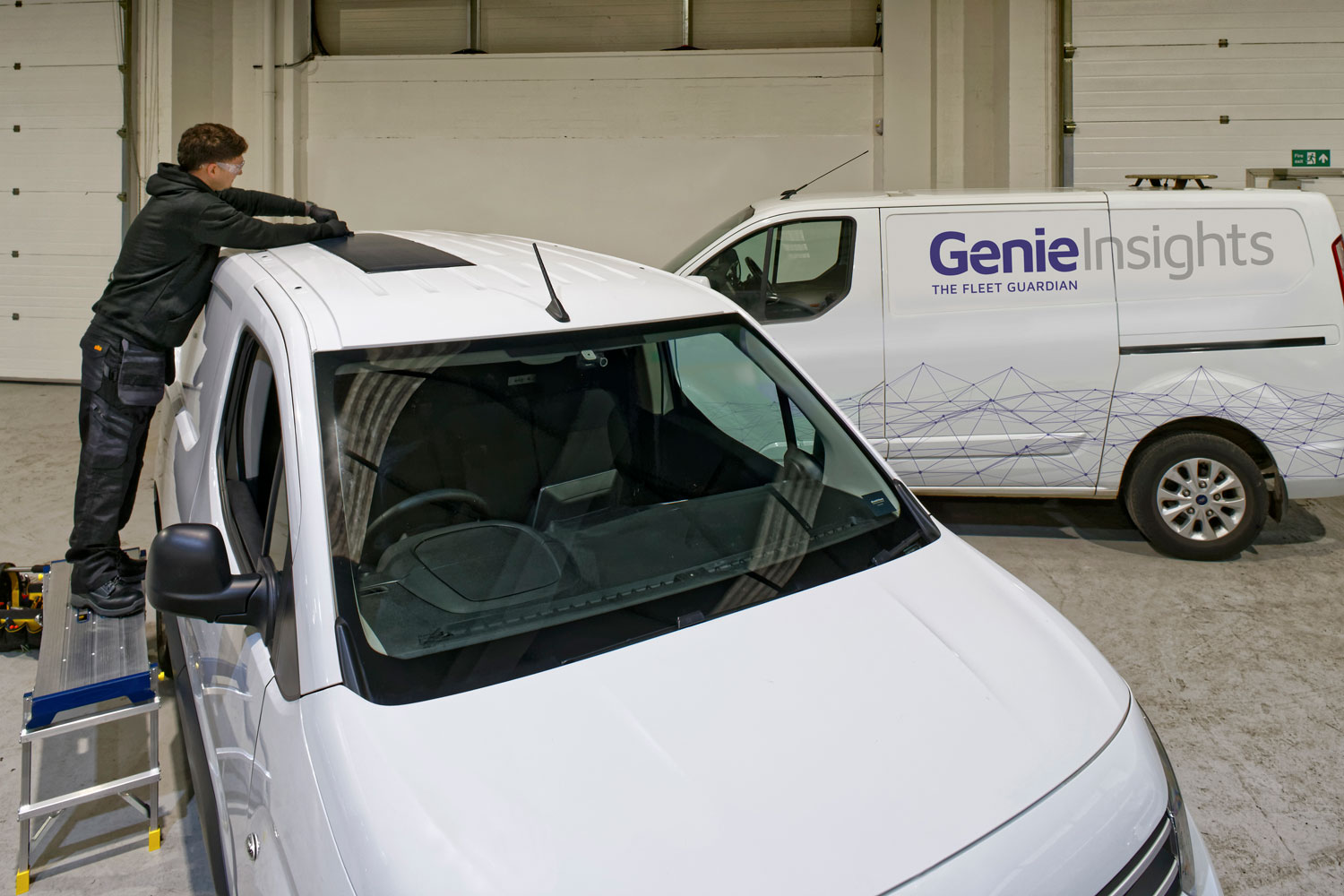 Fitter on a ladder beside a Genie Insights Fleet Guardian van fitting the solar panel